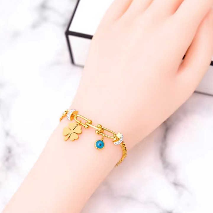 Gold bracelet with a clover and evil eye charm on a wrist against a marble background