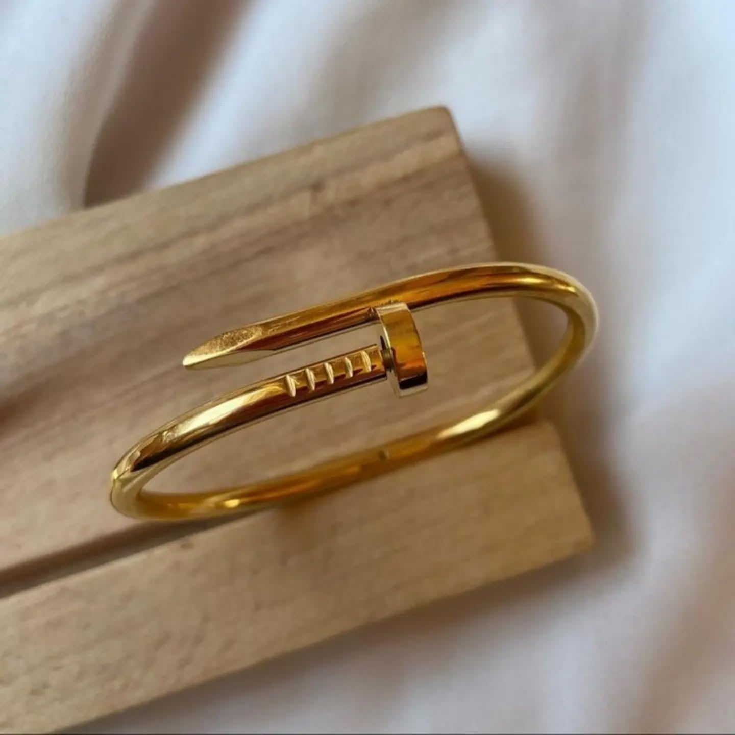 Nail-shaped gold bangle placed on a wooden block