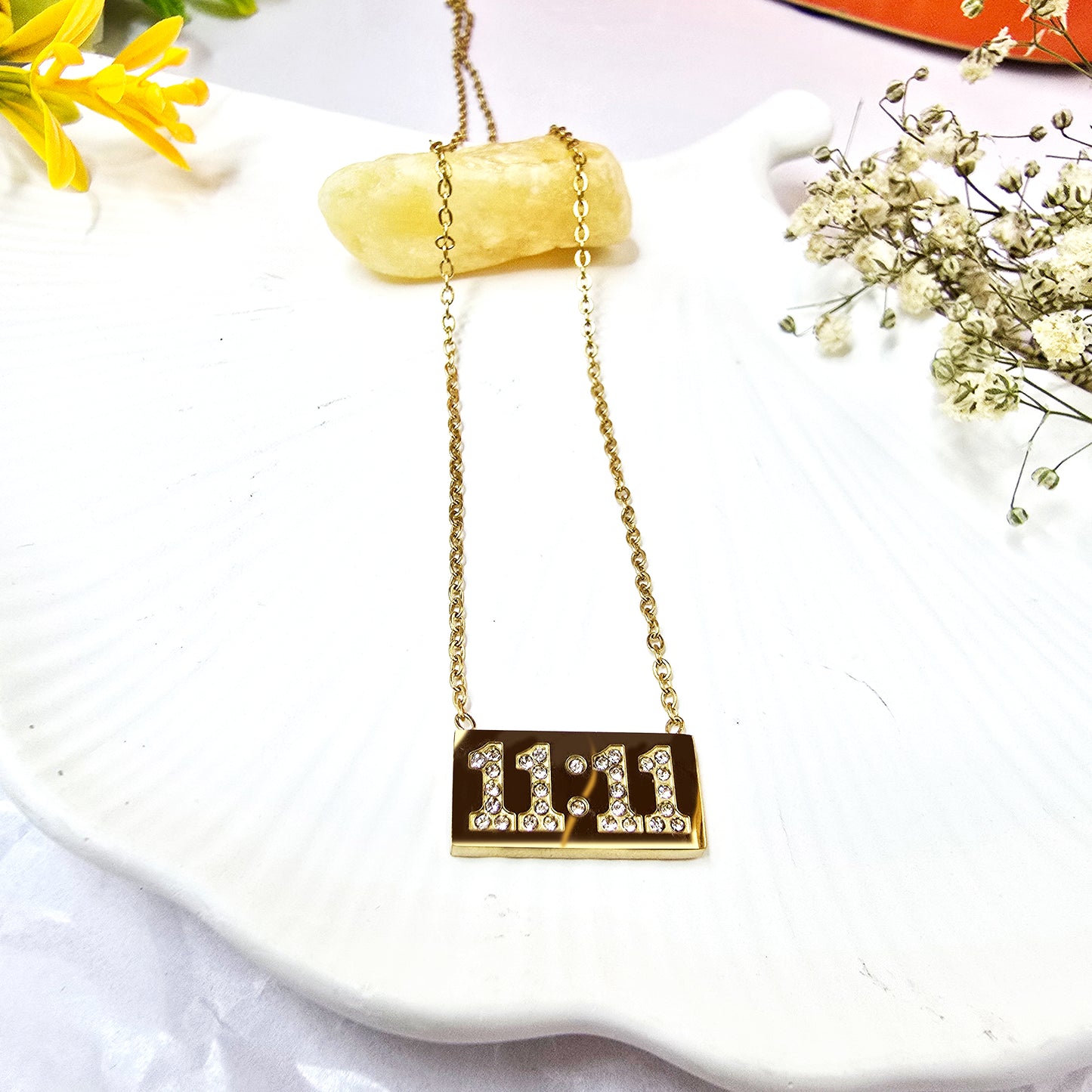 11:11 Pendant Chain on white shell background featuring gold plate with crystal-studded digits.