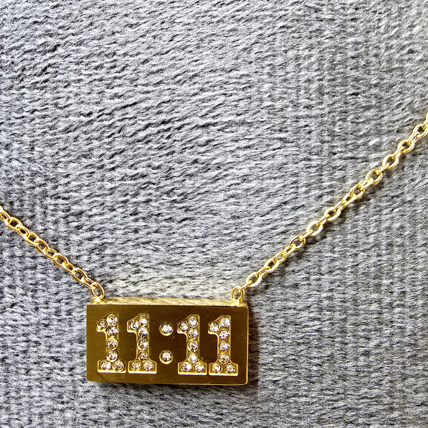Close-up of 11:11 Pendant on grey velvet surface showing gold finish and sparkle.