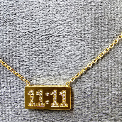 Close-up of 11:11 Pendant on grey velvet surface showing gold finish and sparkle.