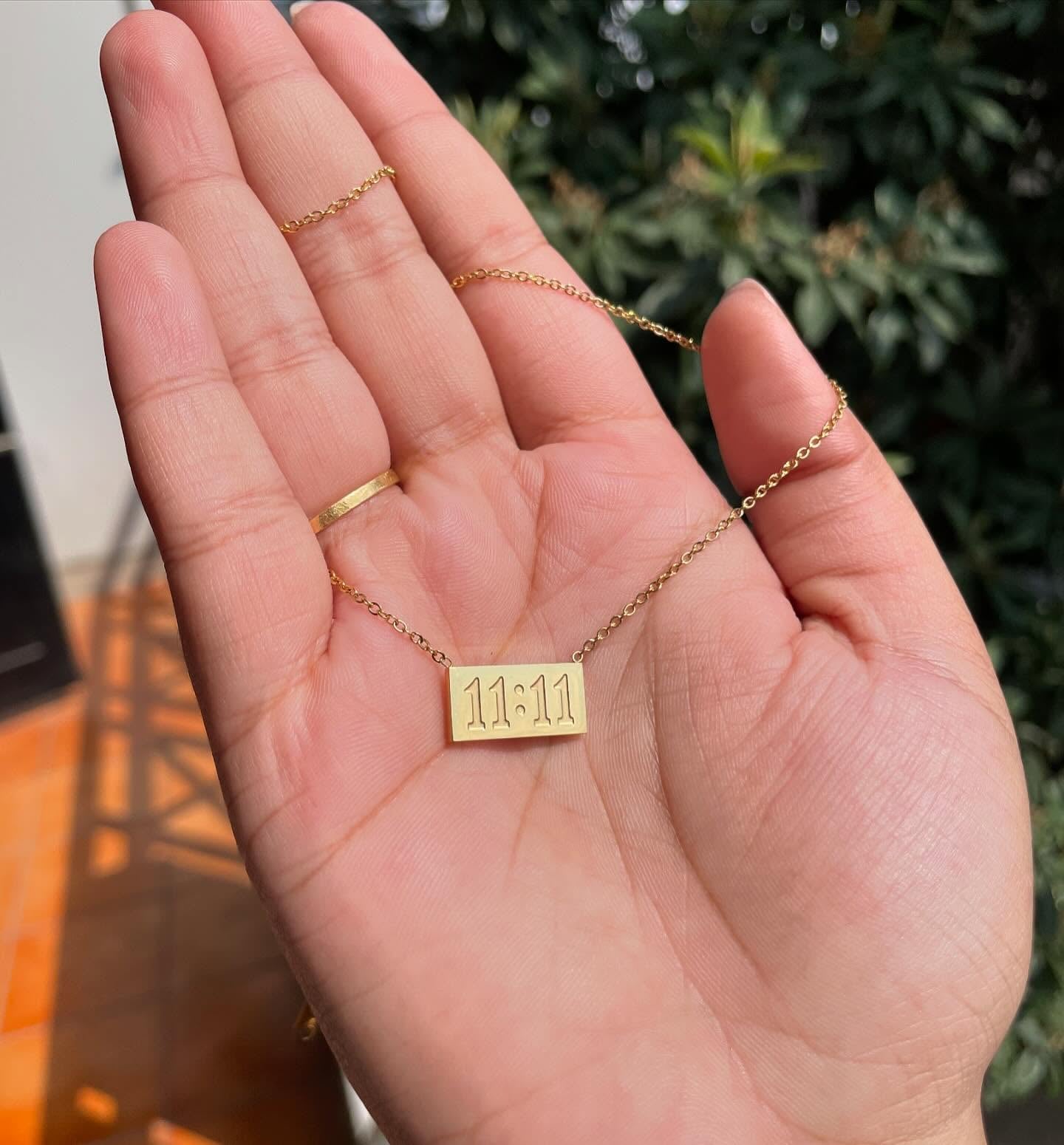 11:11 pendant chain held in hand with sunlight and greenery in the background