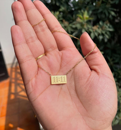 11:11 pendant chain held in hand with sunlight and greenery in the background