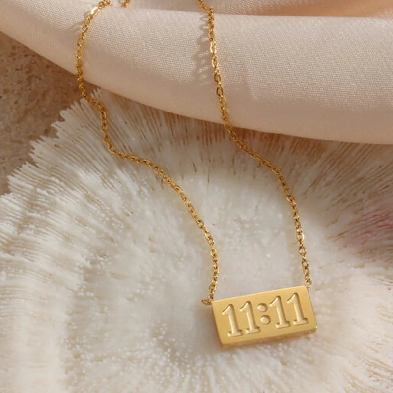 11:11 gold necklace resting on soft blush fabric and coral surface