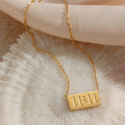 11:11 gold necklace resting on soft blush fabric and coral surface