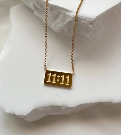 11:11 gold necklace resting on soft blush fabric and coral surface