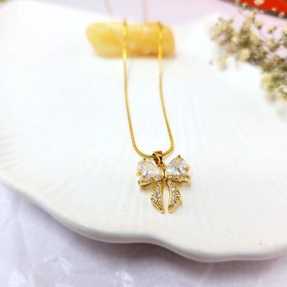 Close-up of AD Bow Necklace on white shell background showing crystal-studded bow pendant.