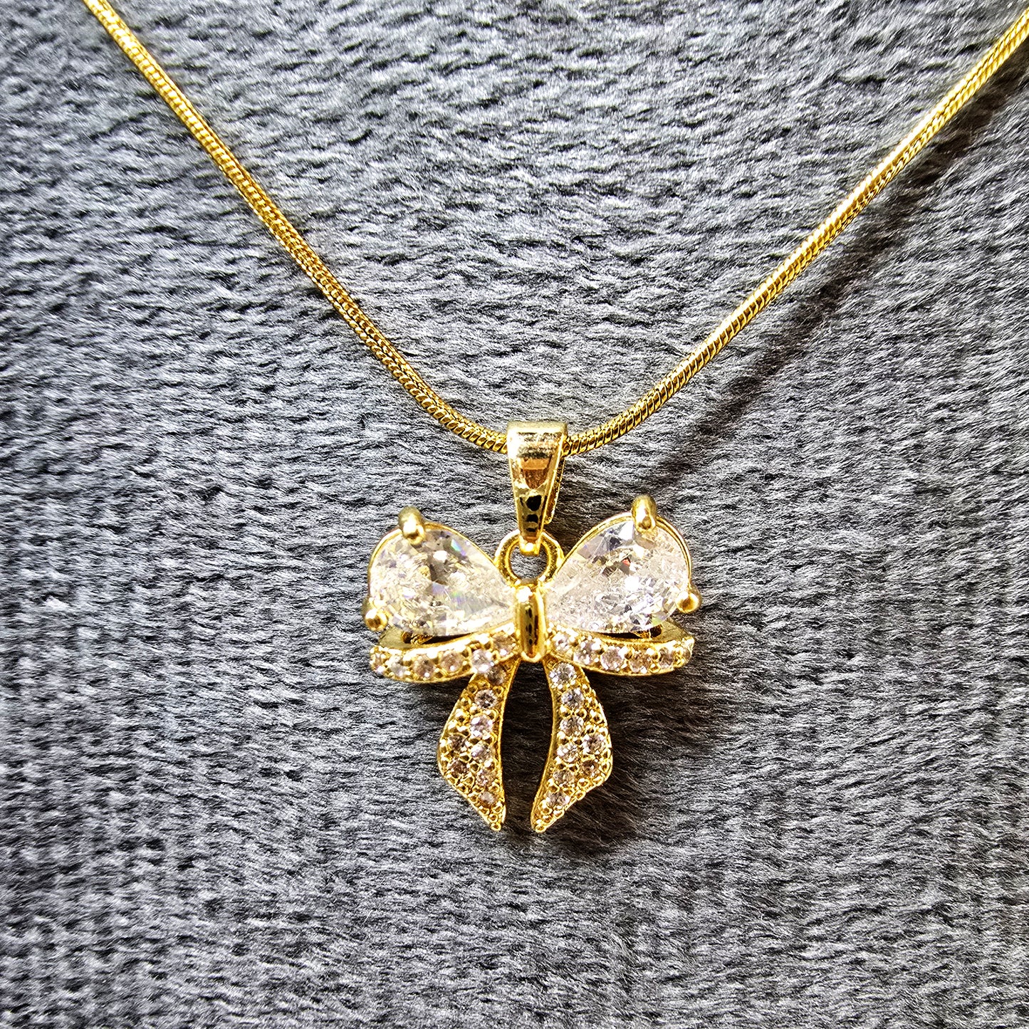 AD Bow Pendant on grey velvet display highlighting sparkle and detailing.