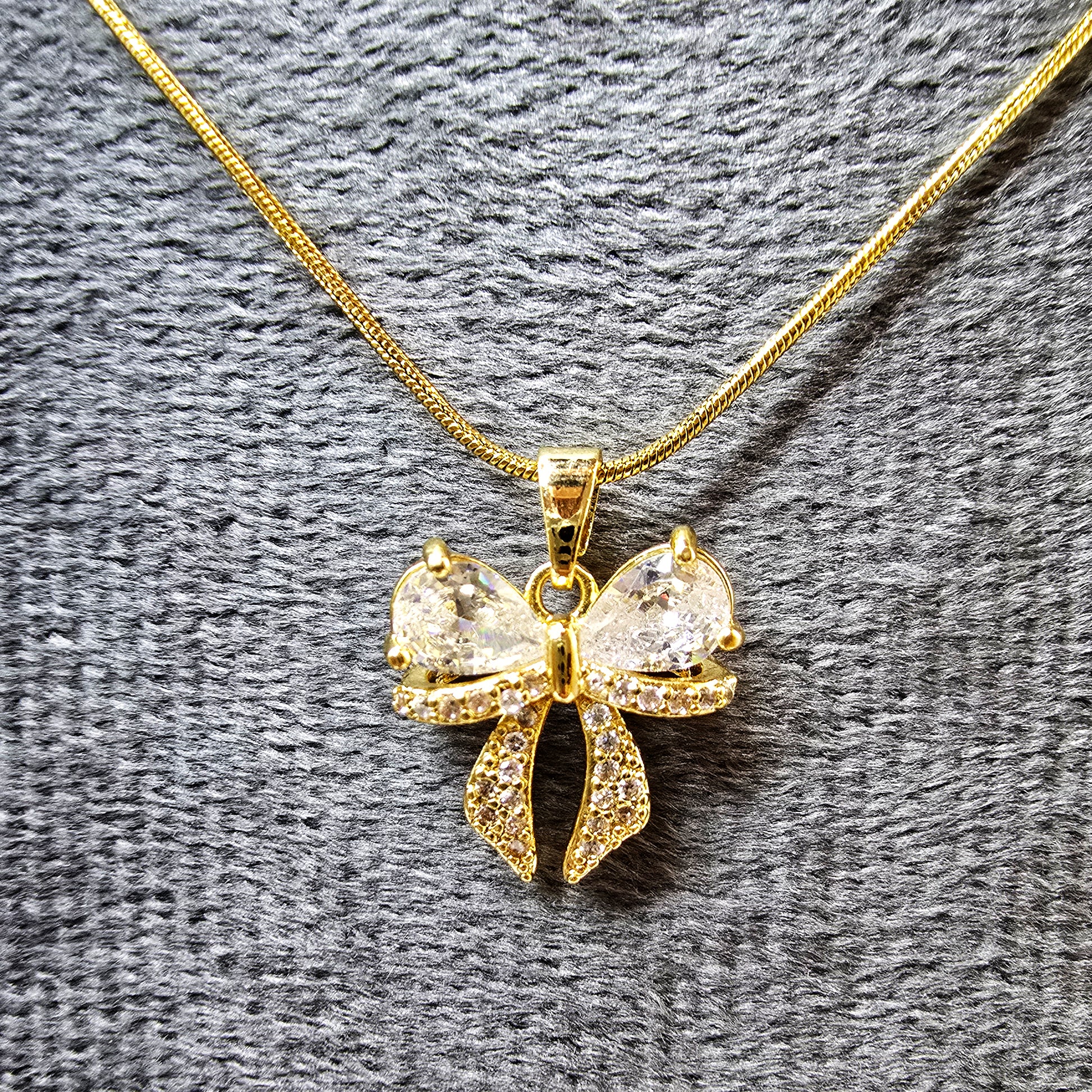 AD Bow Pendant on grey velvet display highlighting sparkle and detailing.