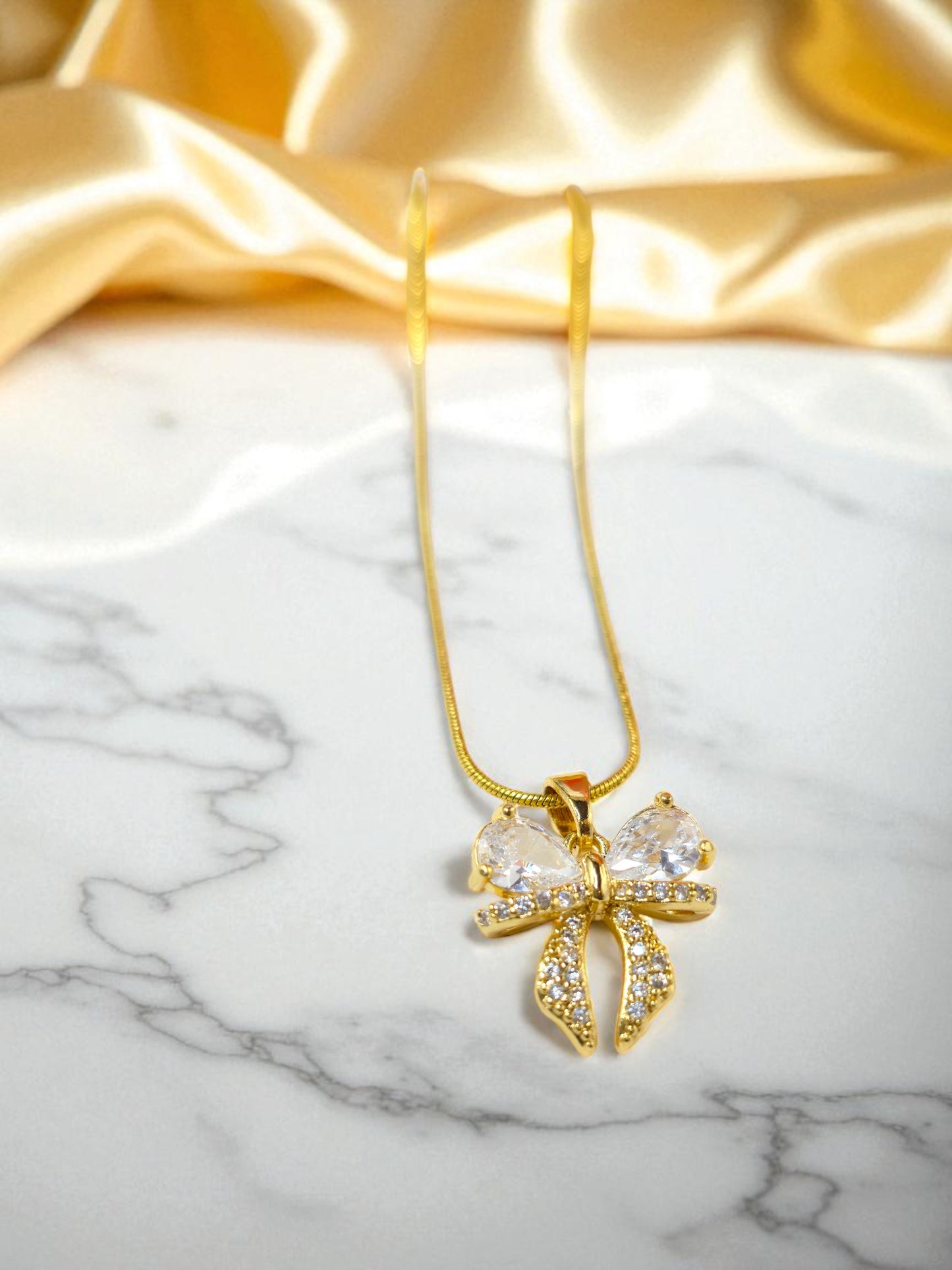 AD Bow Necklace on gold fabric and marble background for luxury presentation.