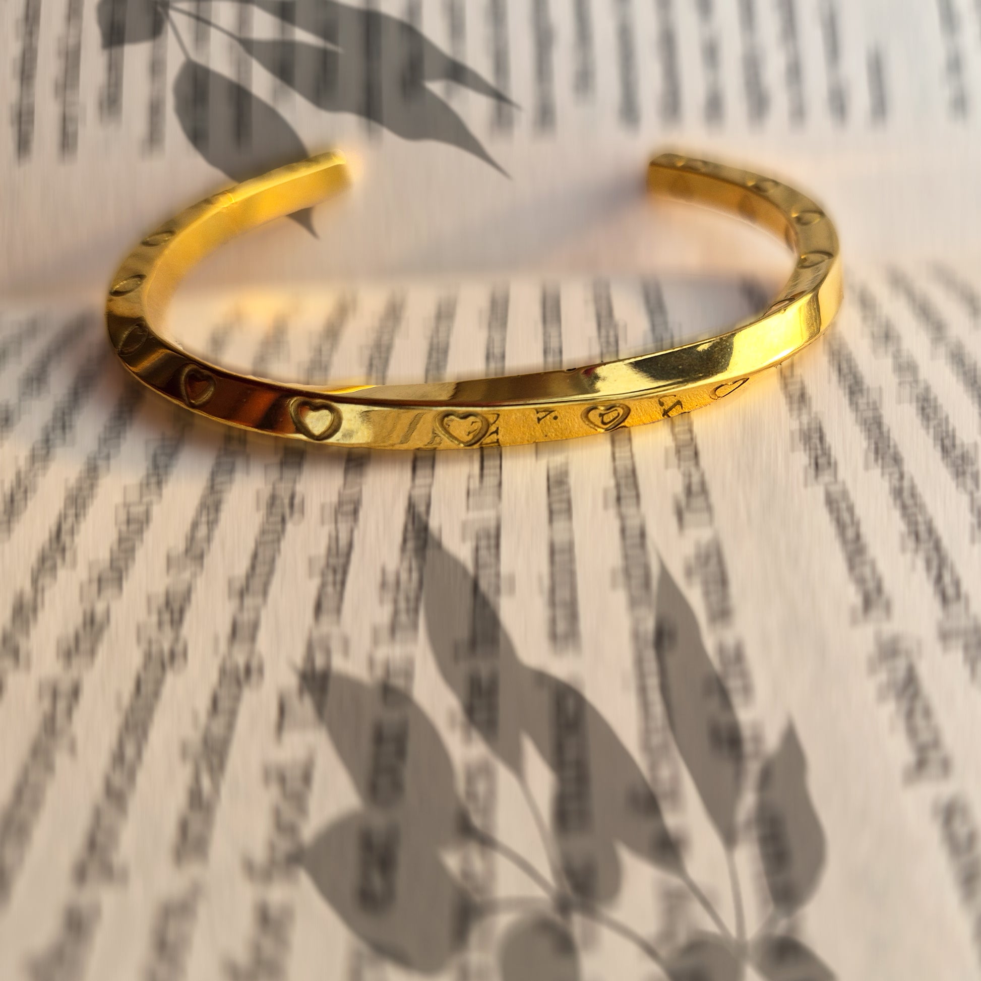 Artistic shot of gold heart-engraved bangle casting shadows on open book pages.