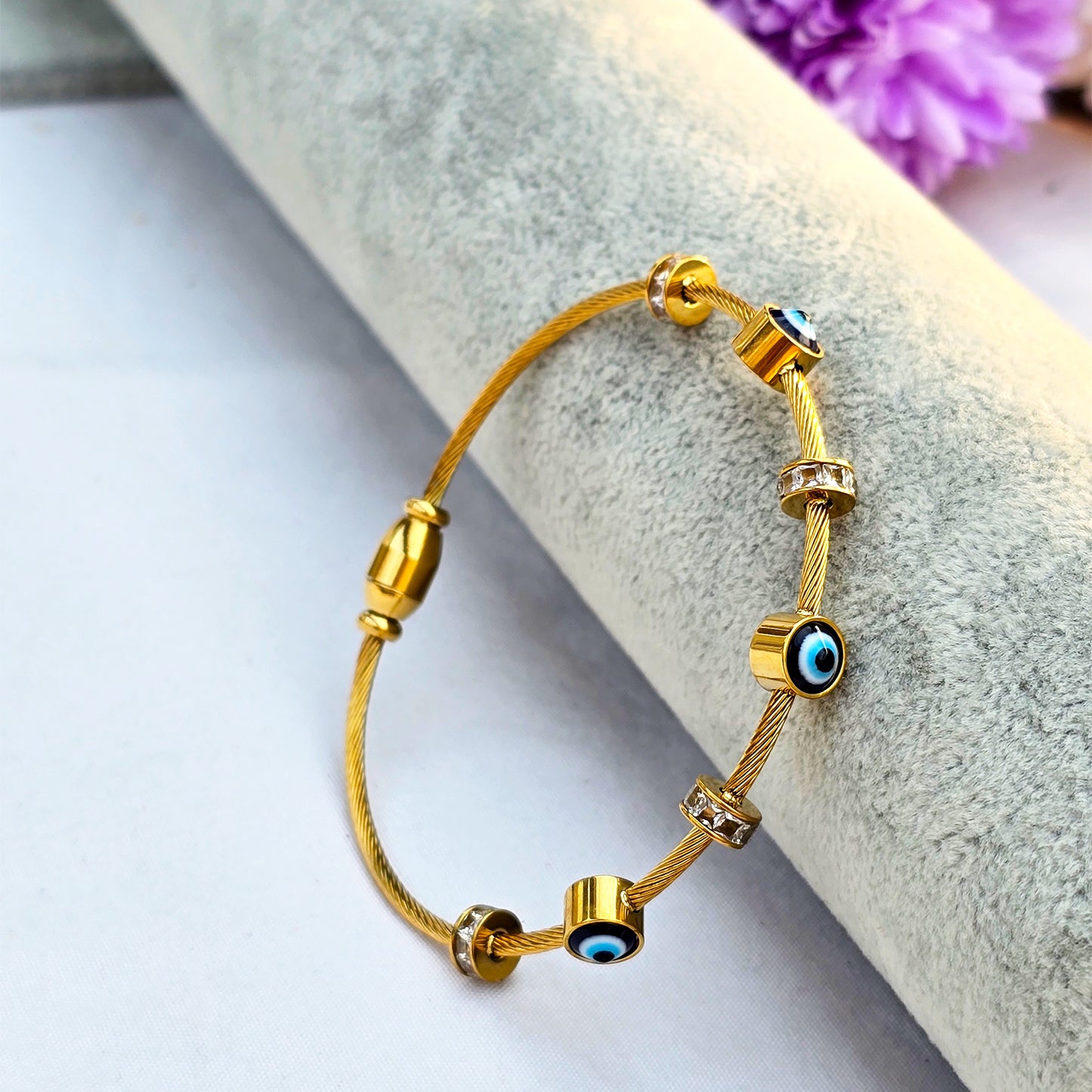 Gold twisted cable wire bangle featuring blue evil eye beads and crystal spacers.