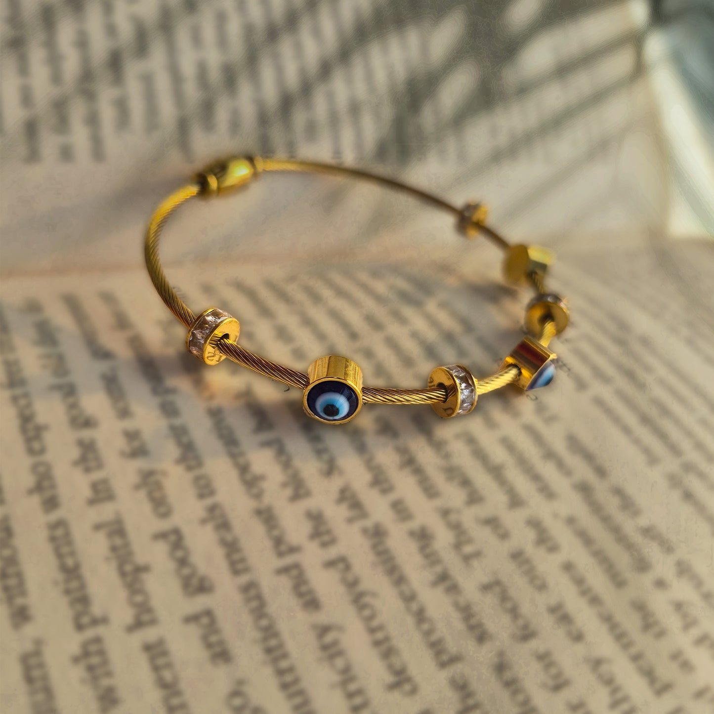 Close-up detail of sliding evil eye and diamond-look charms on a gold wire bangle.