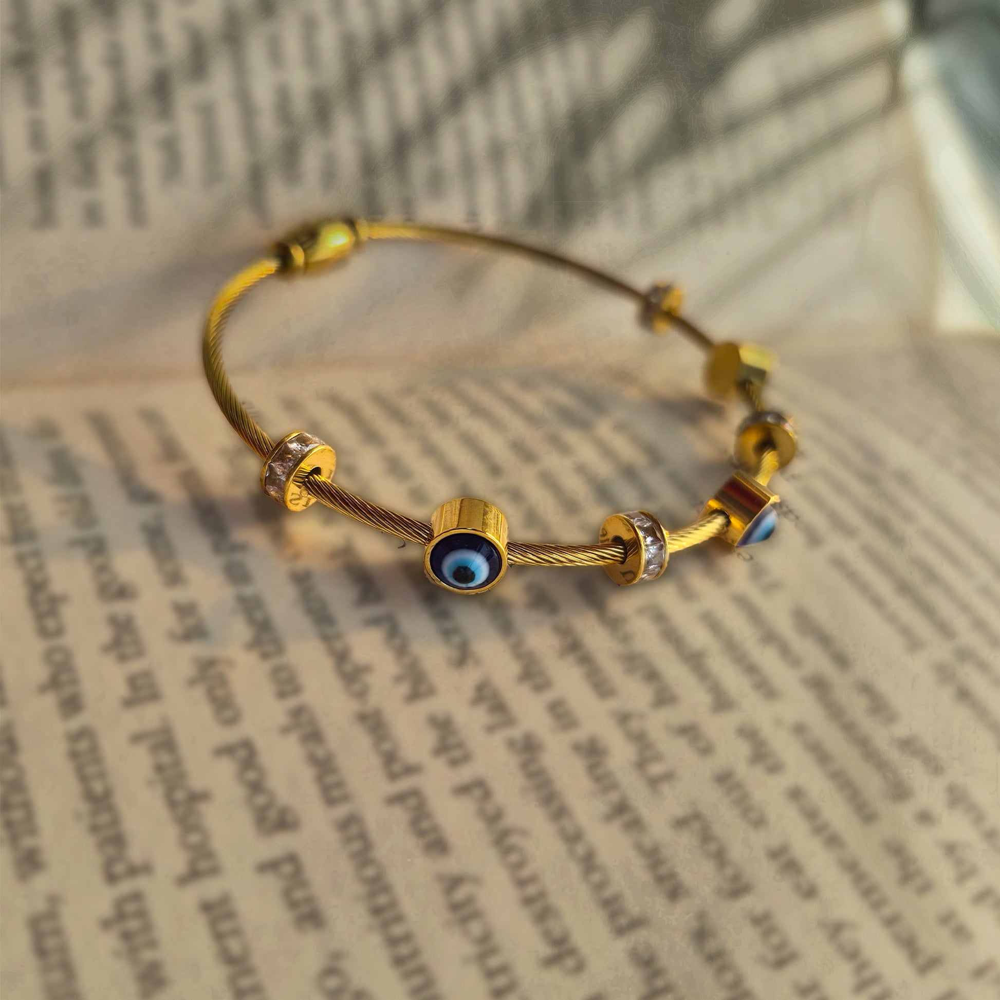 Close-up detail of sliding evil eye and diamond-look charms on a gold wire bangle.
