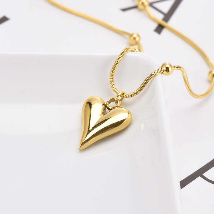 Close-up of shiny teardrop heart pendant on plate with part of chain visible