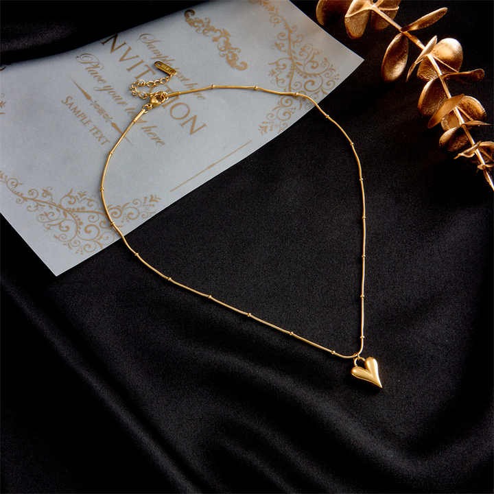 Necklace styled on black silk background beside golden décor and invitation card