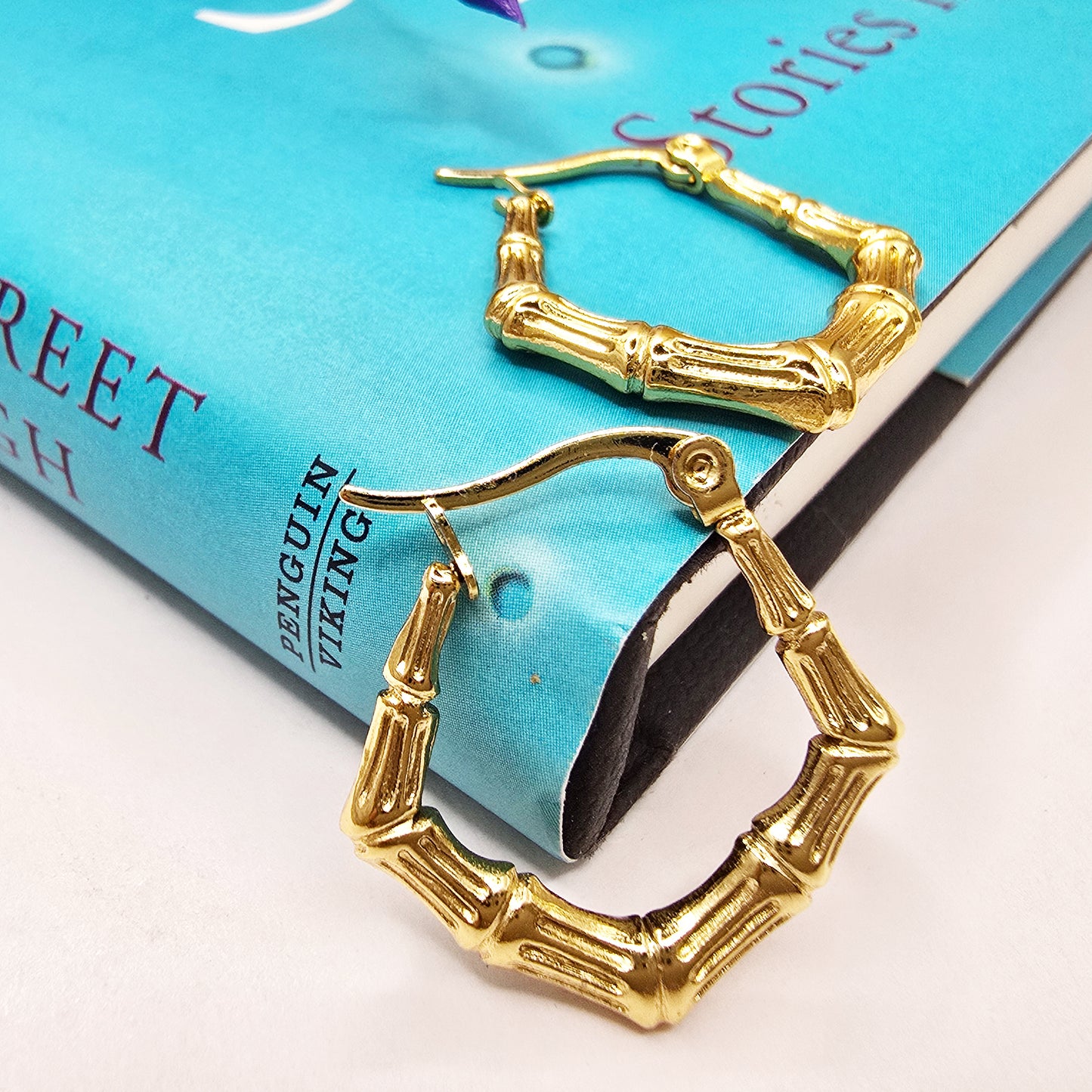 Bamboo Luxe Earrings – bold gold hoops placed on a blue book
