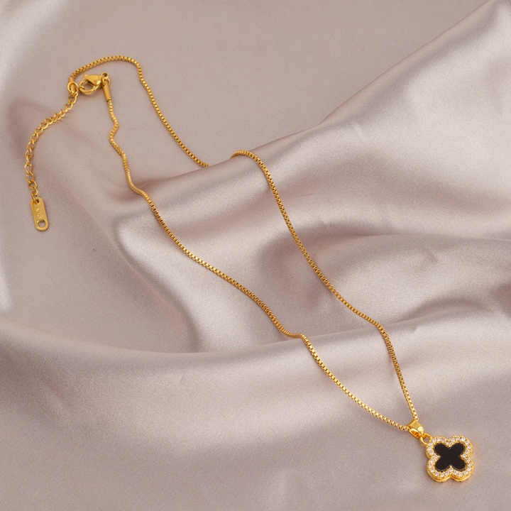 Full view of gold clover necklace with chain laid out on a satin fabric