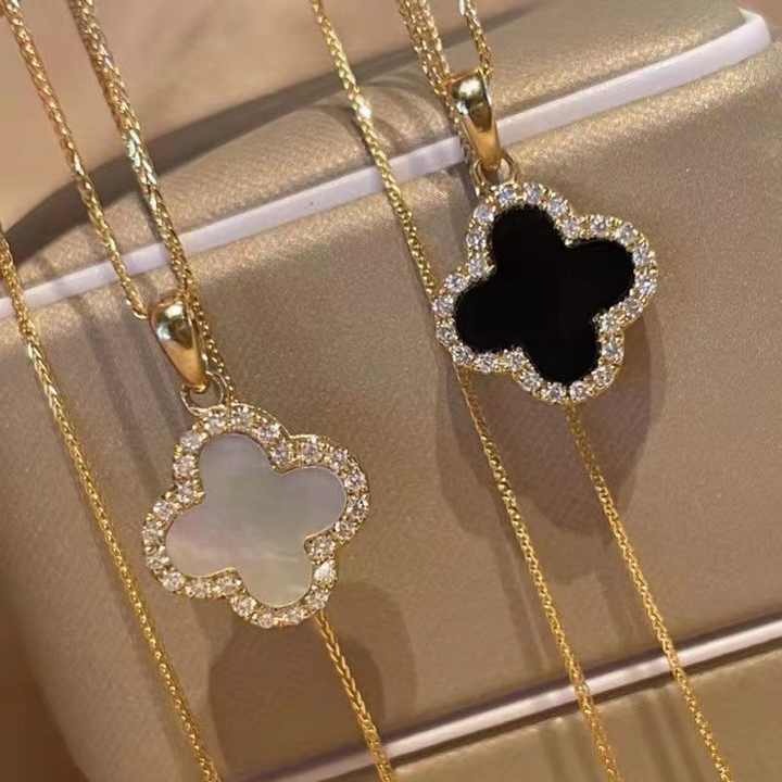 Two gold necklaces with clover-shaped pendants on a beige surface.