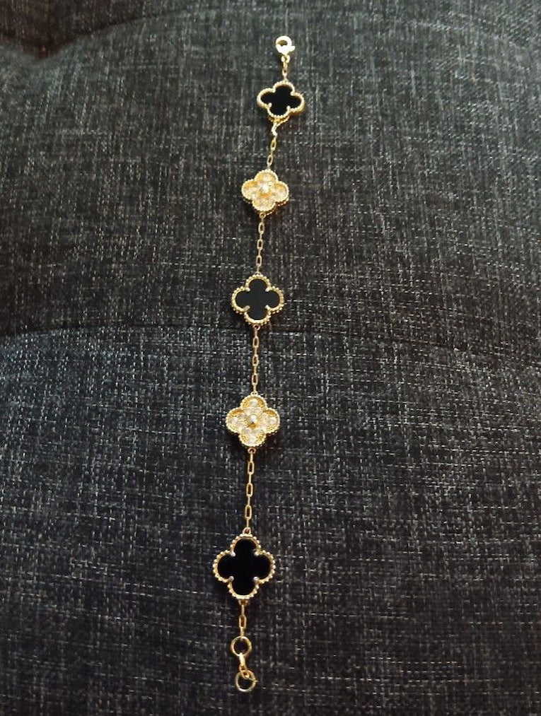 Gold bracelet with clover-shaped charms on a dark textured fabric background