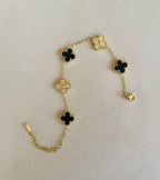 Gold bracelet with alternating black clover and crystal charms laid flat on neutral background