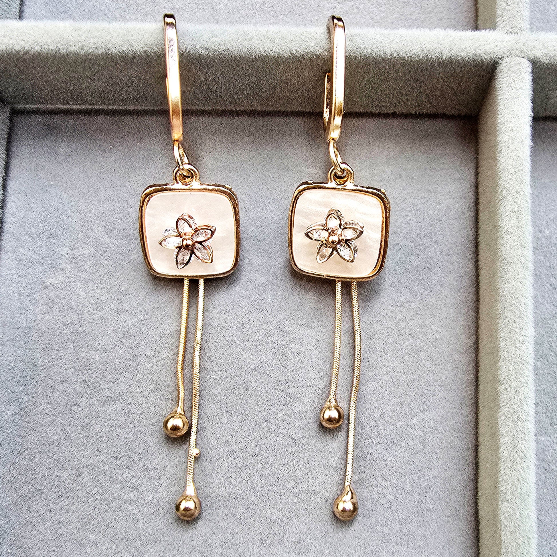 A pair of gold-toned Blush Drop earrings with floral centers and long chain dangles in a grey jewelry organizer.