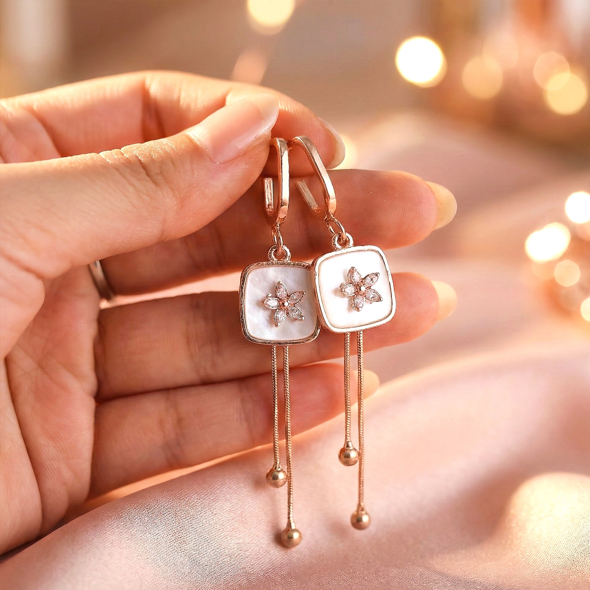 Aesthetic photography of the Blush Drop earrings on pink silk fabric with warm, glowing bokeh lights.