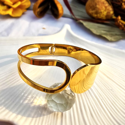 Artistic flat lay of gold geometric cuff bracelet on a white shell tray.