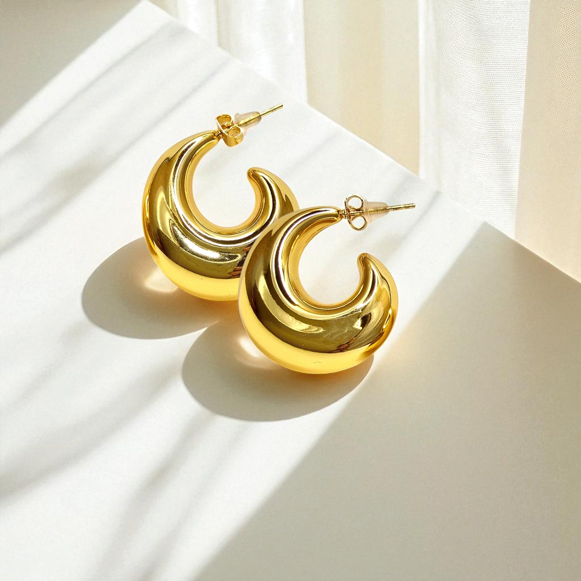 Bold Loop Earrings on white surface in natural light, glossy gold finish