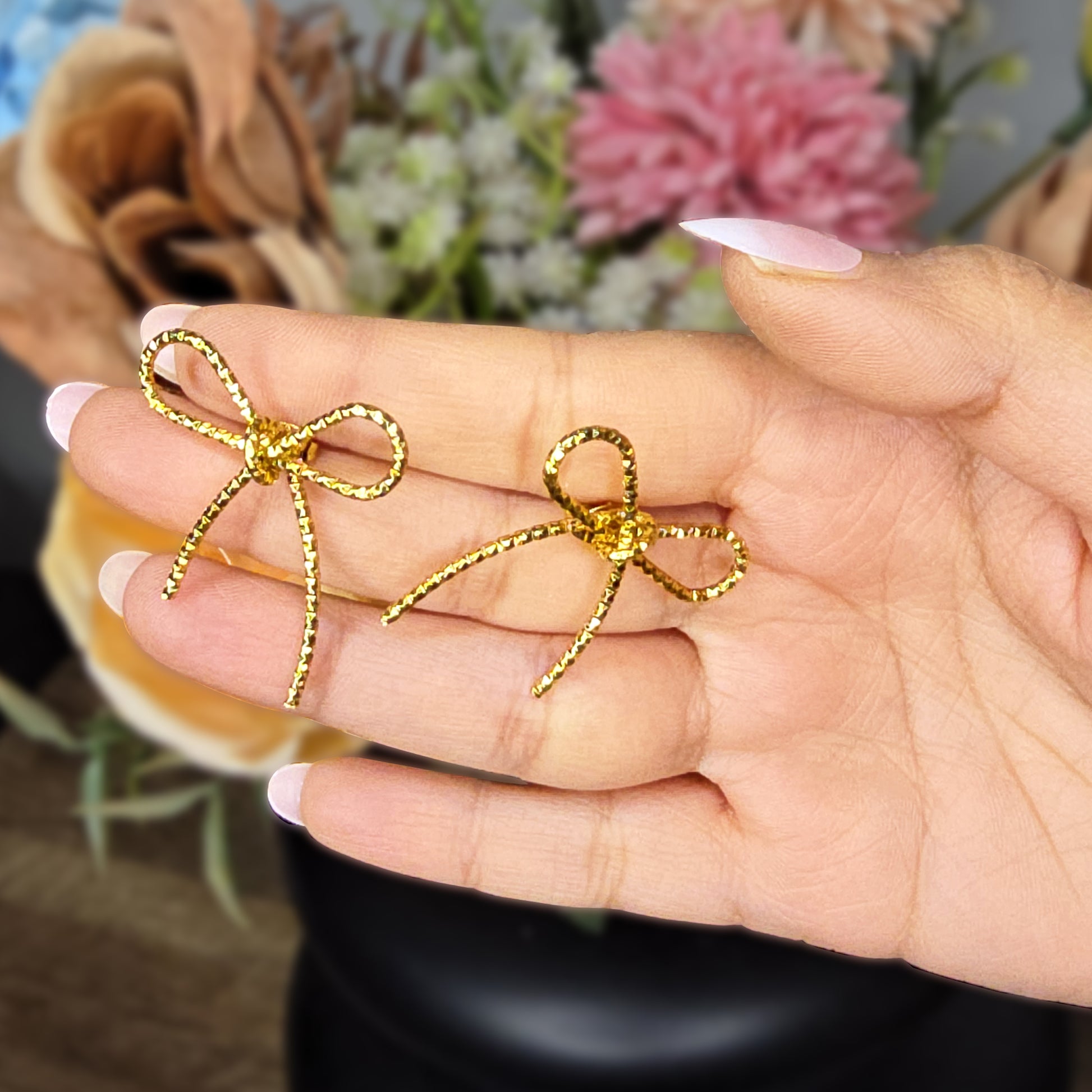 Hand holding a pair of gold anti-tarnish bow knot earrings to show size and scale.