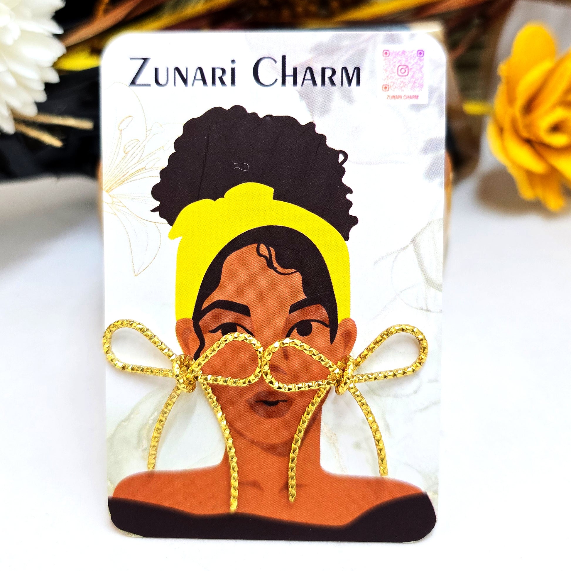 Gold bow knot stud earrings displayed on Zunari Charm branded packaging card with illustration.