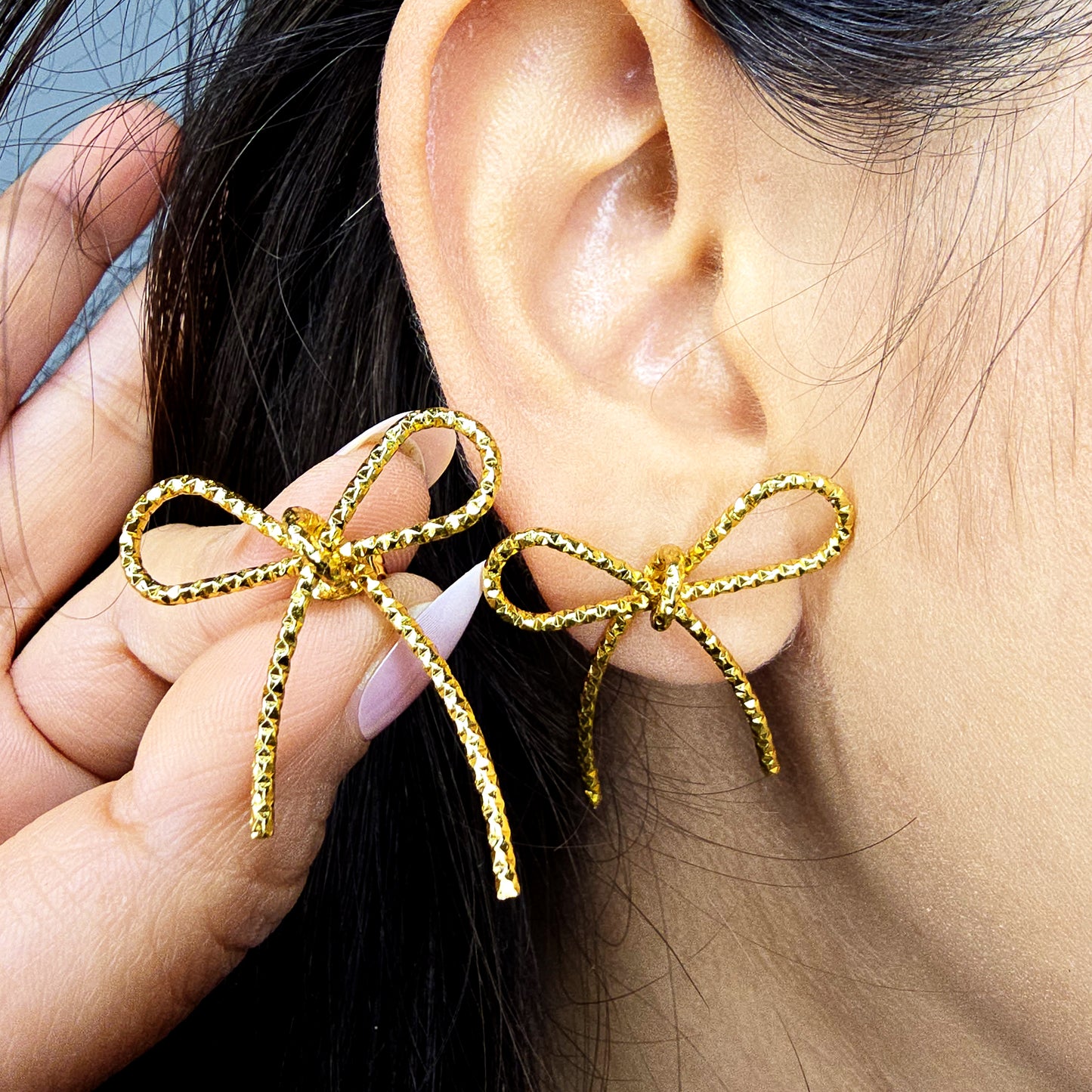Side profile of model wearing gold textured bow knot stud earrings showing fit on the earlobe.