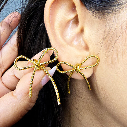 Side profile of model wearing gold textured bow knot stud earrings showing fit on the earlobe.
