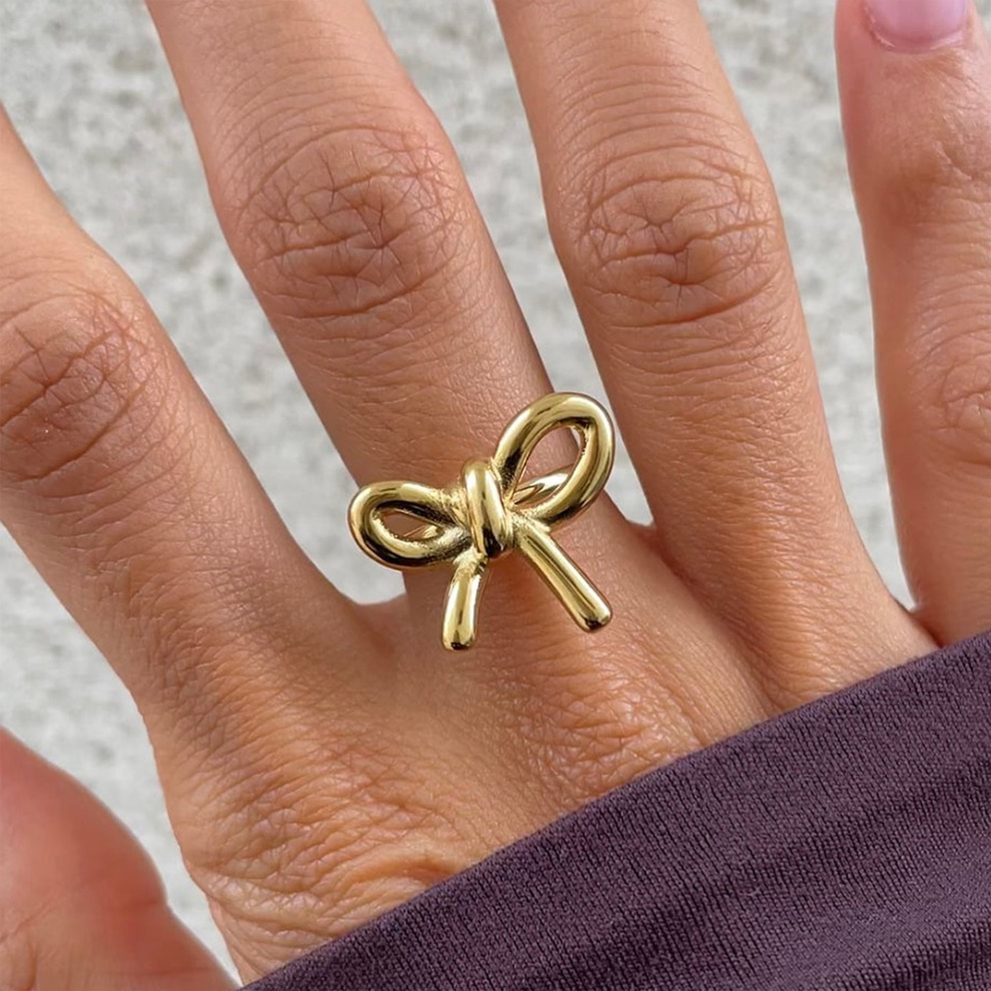 Gold bow knot statement ring worn on finger, highlighting chic ribbon-inspired design – Zunari Charm fashion jewelry.