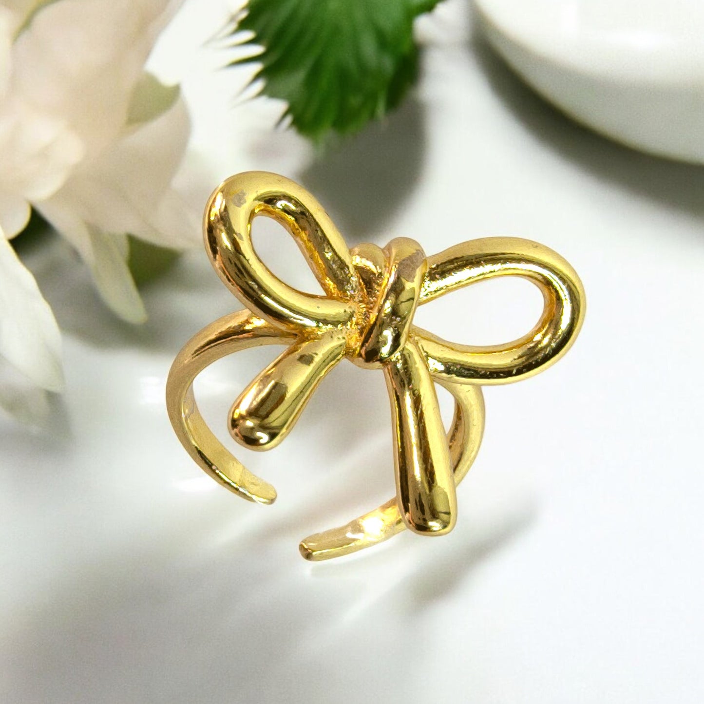 Gold bow knot adjustable ring with ribbon style, photographed on white background with floral accent – Zunari Charm premium jewelry.