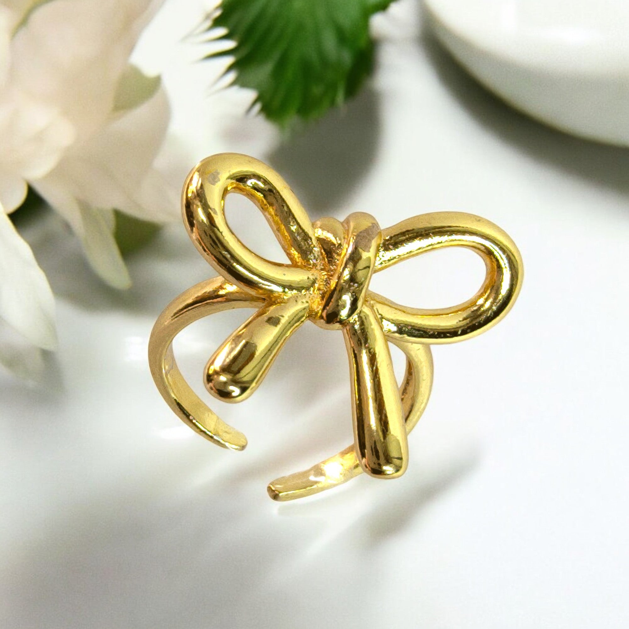 Gold bow knot adjustable ring with ribbon style, photographed on white background with floral accent – Zunari Charm premium jewelry.