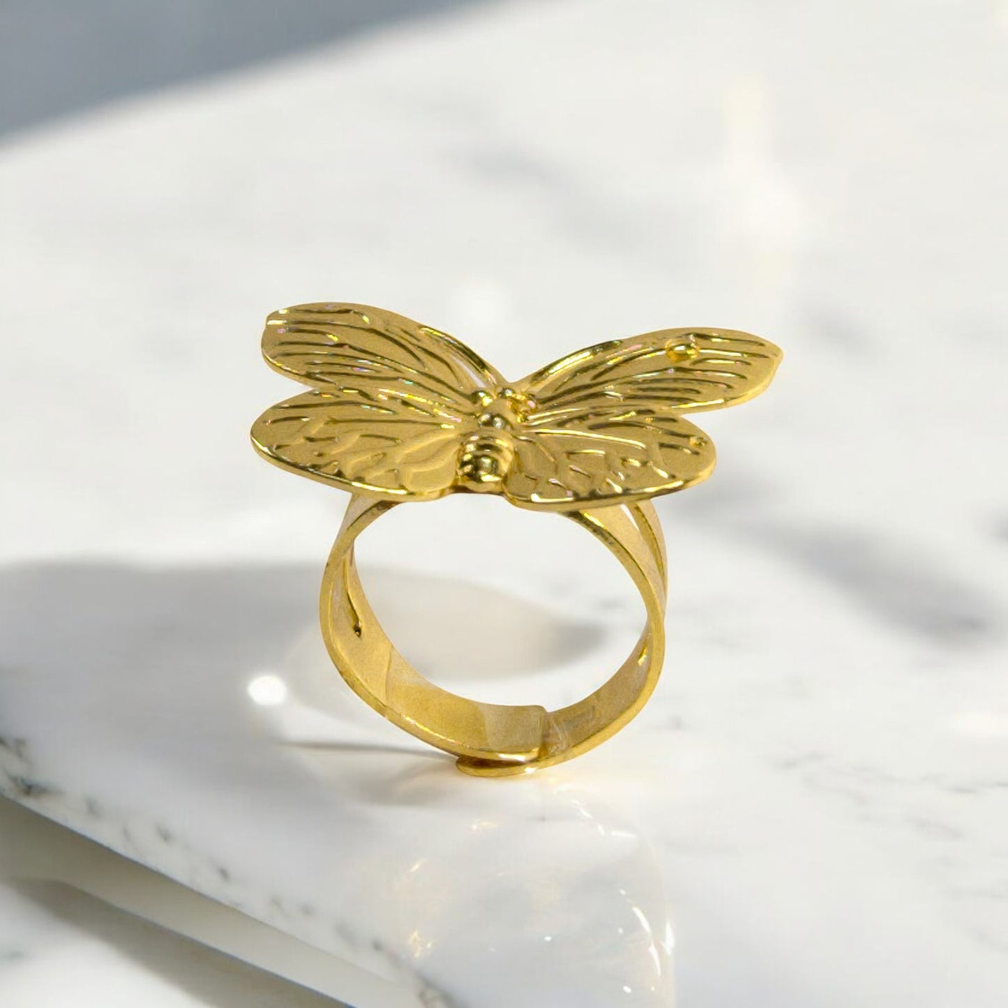 Gold butterfly statement ring with detailed wings, displayed upright on a white marble surface – Zunari Charm jewelry.