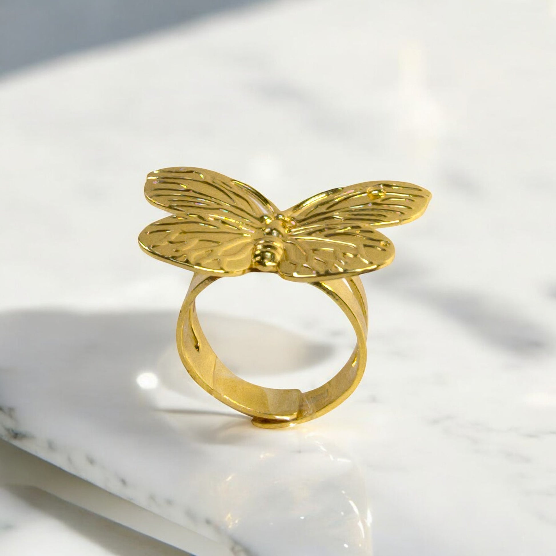 Gold butterfly statement ring with detailed wings, displayed upright on a white marble surface – Zunari Charm jewelry.