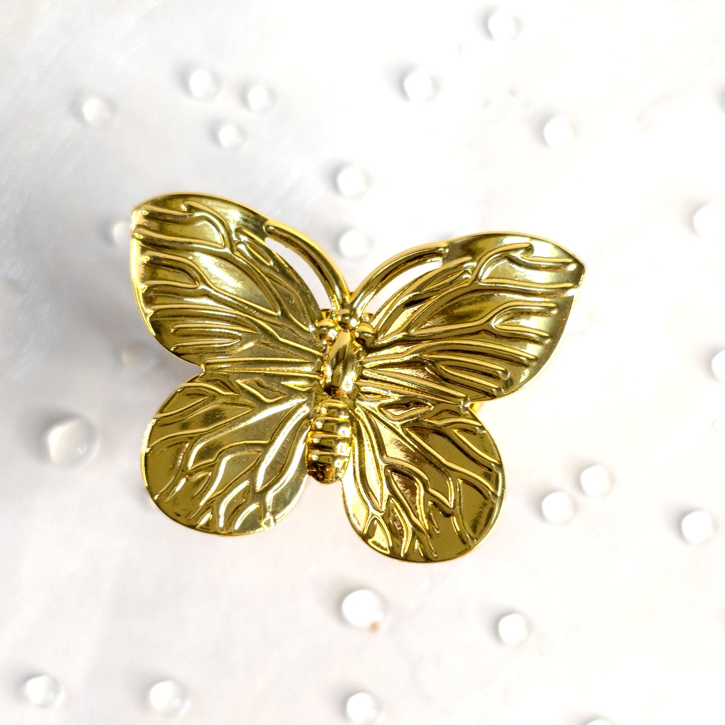 Close-up of gold butterfly ring with textured wing design, showcased on a white surface with water droplets – Zunari Charm statement ring.