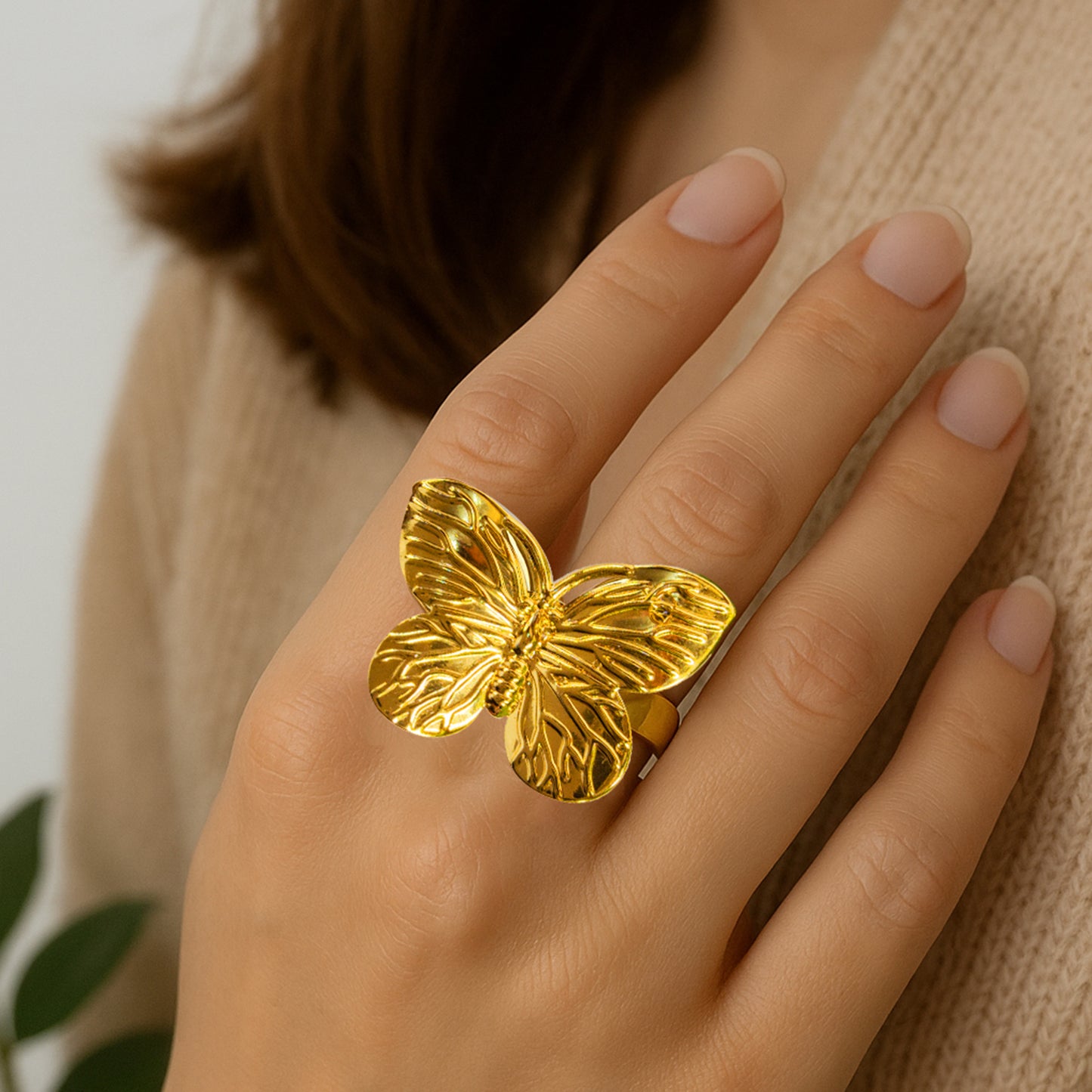 Gold butterfly statement ring worn on a woman’s hand, highlighting bold textured wings against a neutral outfit – Zunari Charm fashion jewelry.