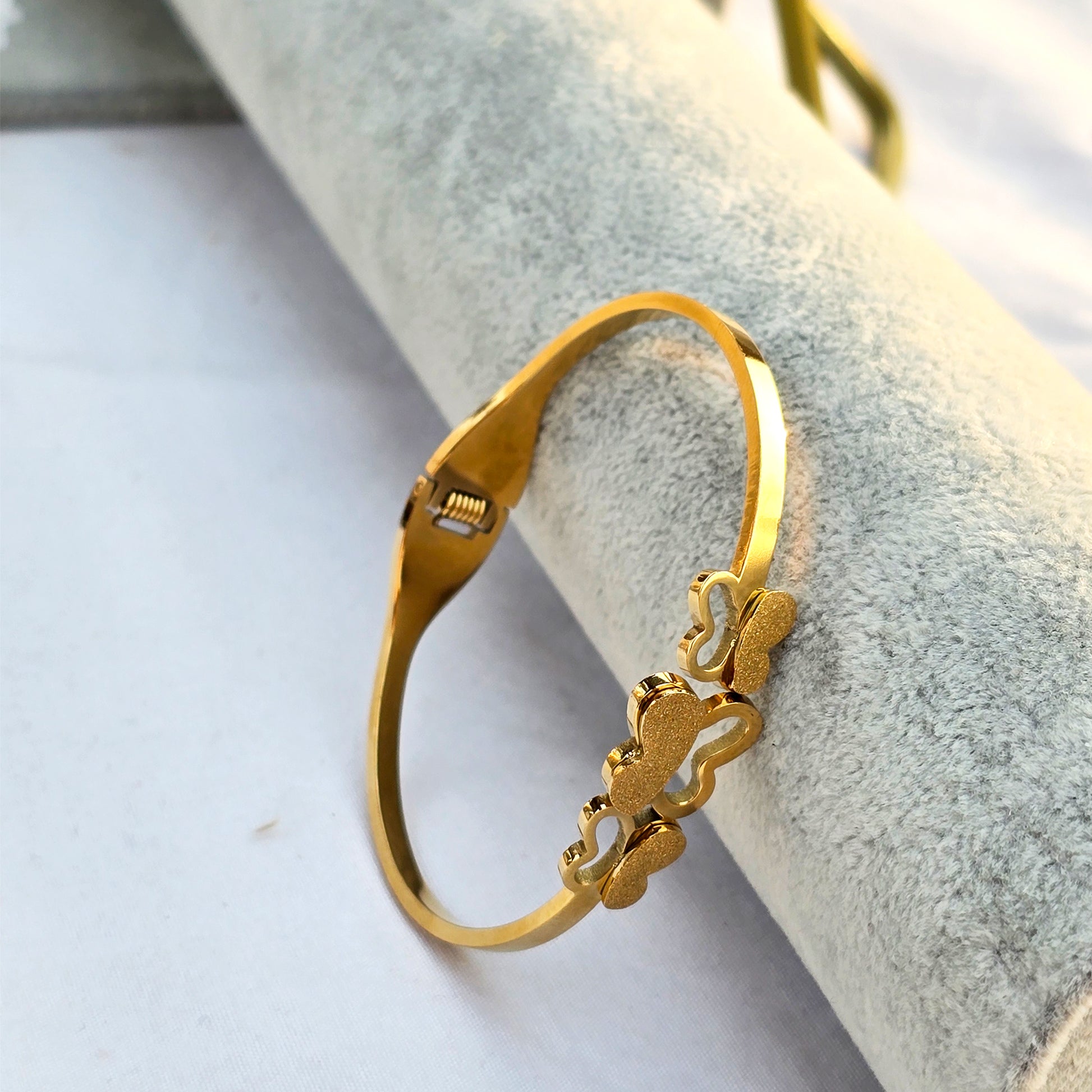 Side view of gold hinged bangle featuring three matte finish butterfly charms.