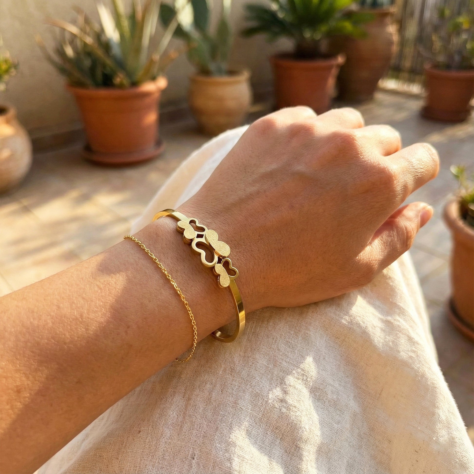 Woman wearing triple butterfly gold bangle stacked with a thin gold chain.