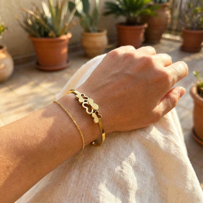 Woman wearing triple butterfly gold bangle stacked with a thin gold chain.