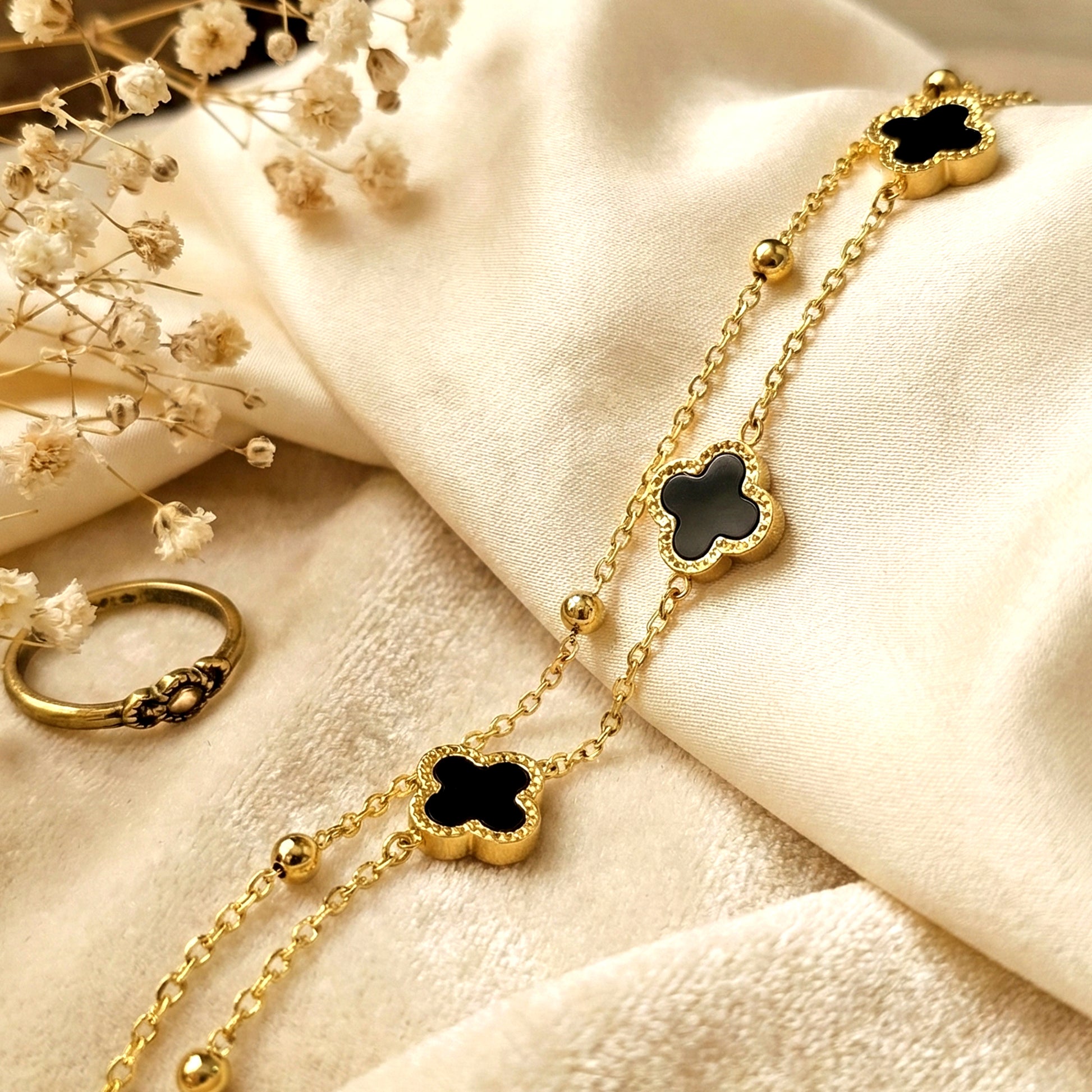 Black clover layered bracelet on soft satin fabric with gold chain detailing elegant waterproof jewelry