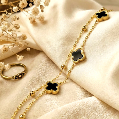 Black clover layered bracelet on soft satin fabric with gold chain detailing elegant waterproof jewelry