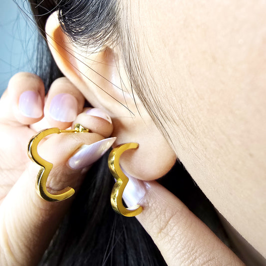 Macro shot of a woman wearing the gold Crest hoop earring, highlighting the unique wave-like shape against the earlobe.