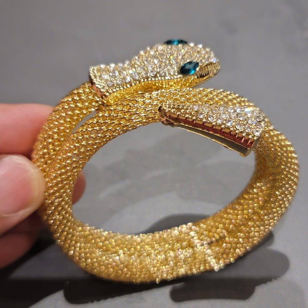 Hand-holding crystal-studded snake bracelet with teal eyes, side angle