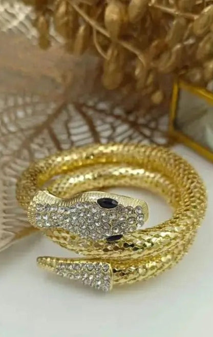 Coiled gold snake bracelet placed on decorative surface with leaf decor