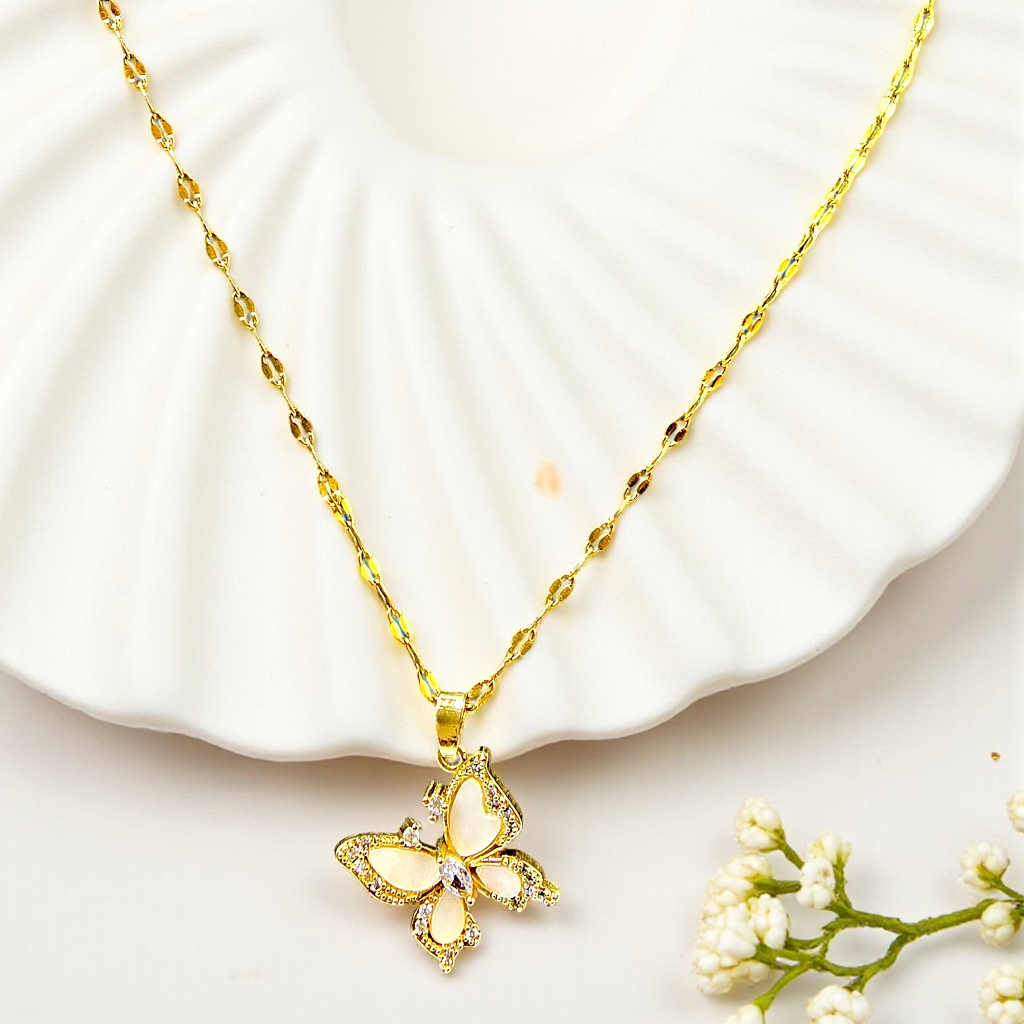 Flatlay of Crystal Butterfly Pendant Chain on white shell plate – gold necklace with floral decor