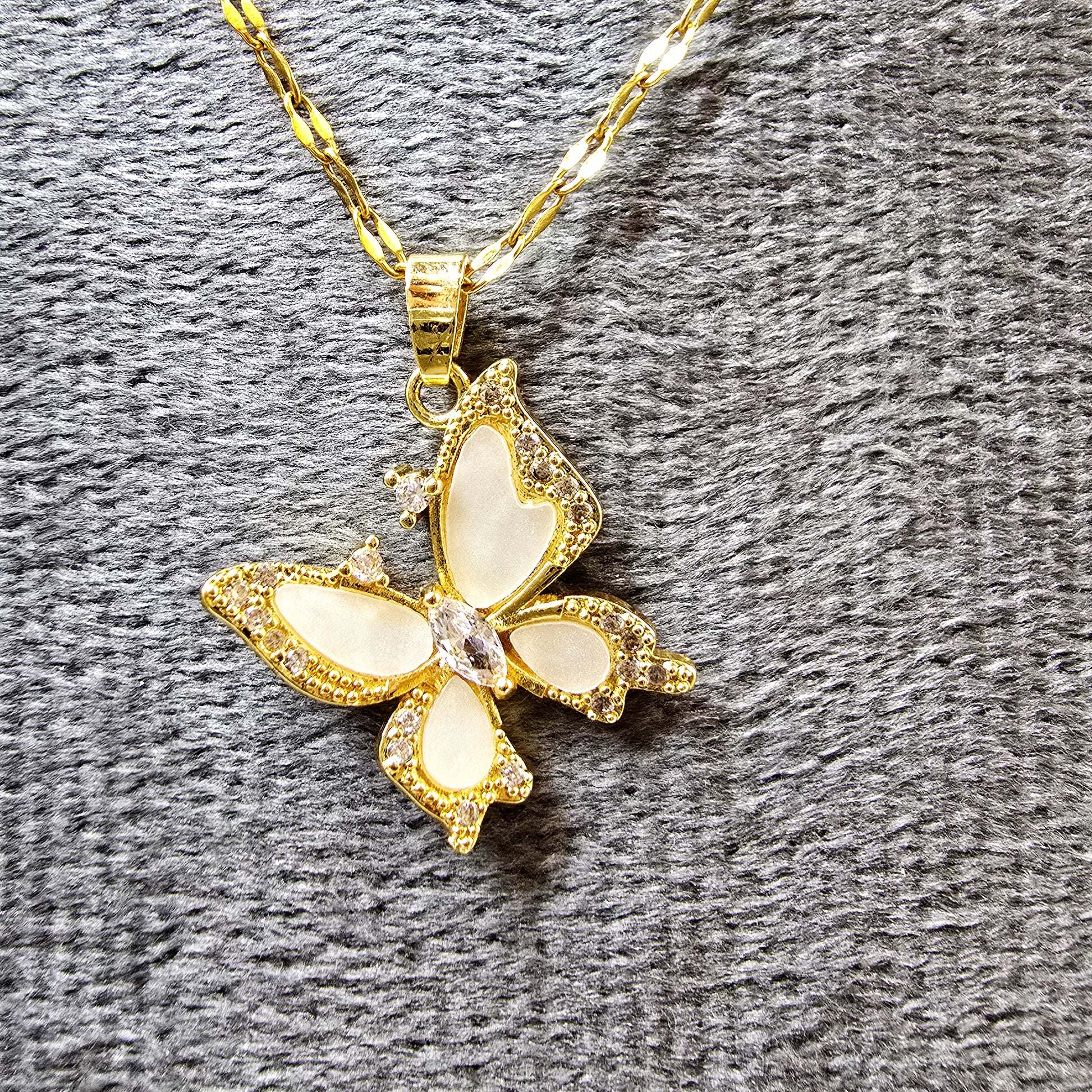 Close-up of butterfly pendant showing crystal and enamel details on grey background